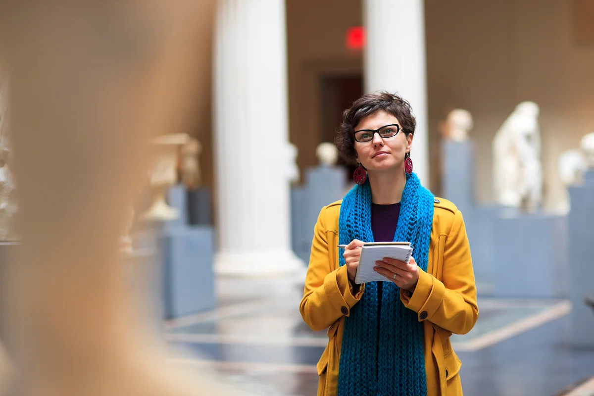 Woman in museum takes notes as she is looking at fine art statue.