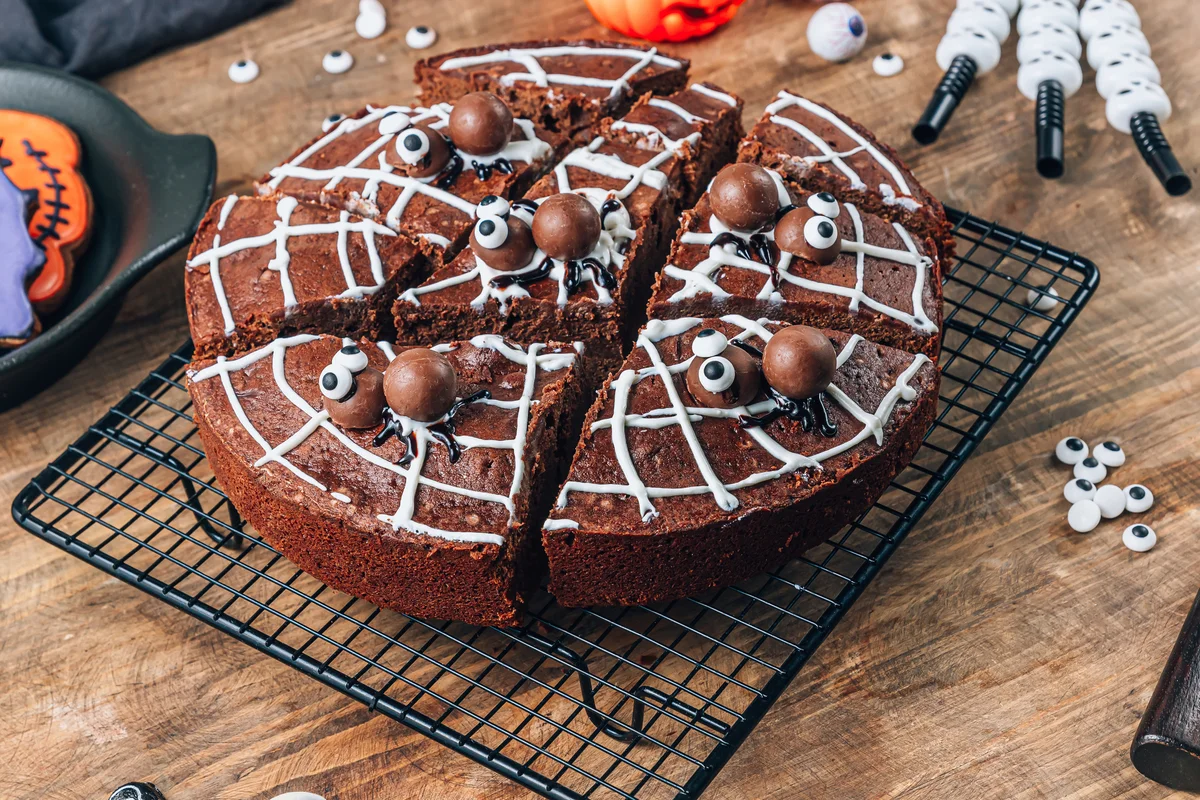 Chocolate cobweb brownies with candy spiders, homemade treats for Halloween on rustic wooden background
