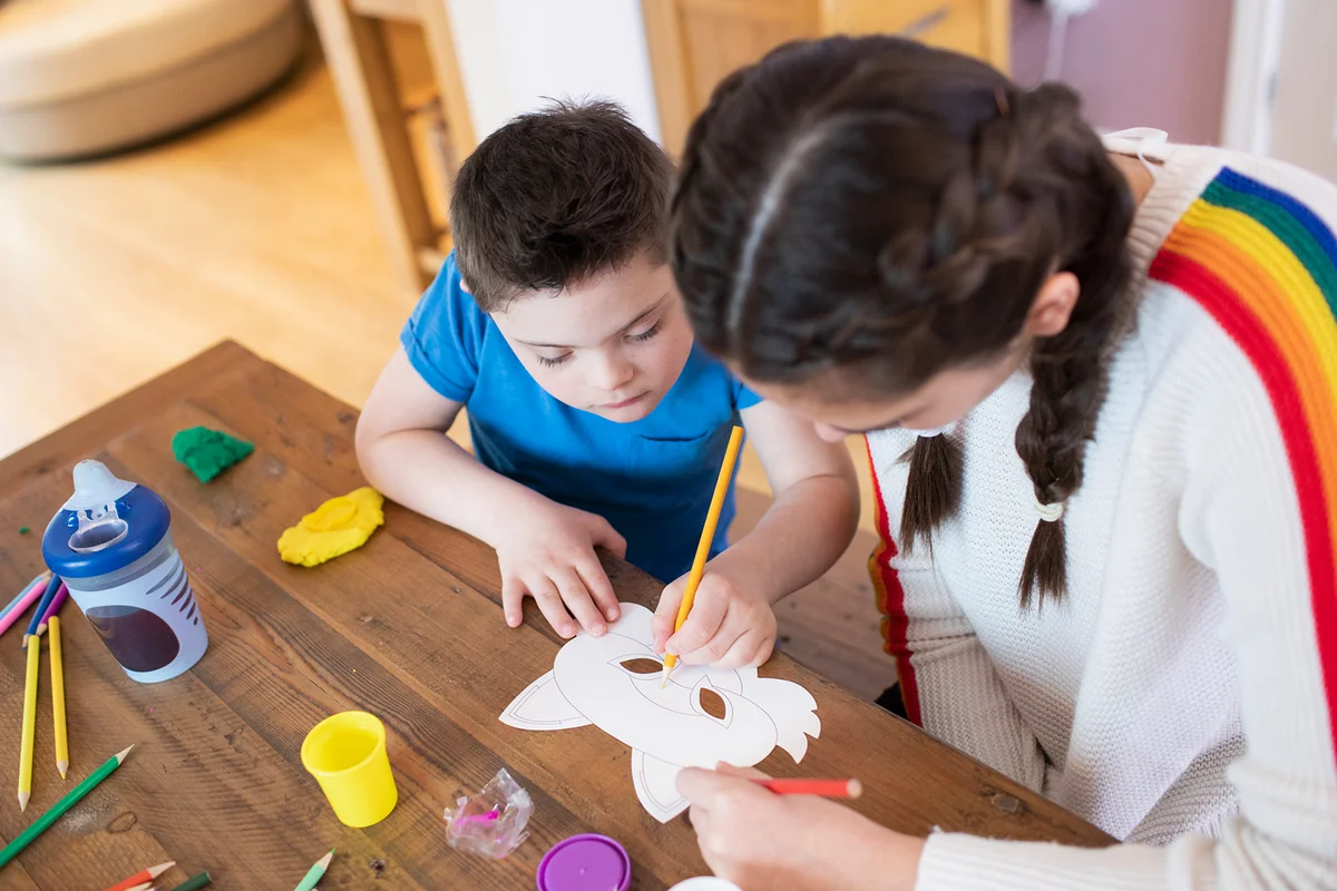 Girl helping brother with Down Syndrome color at table