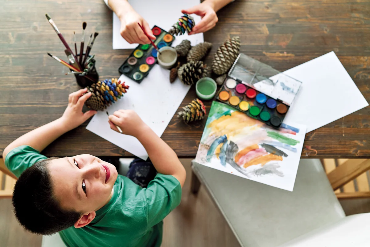Cute family is painting pine cone with watercolor together at home.