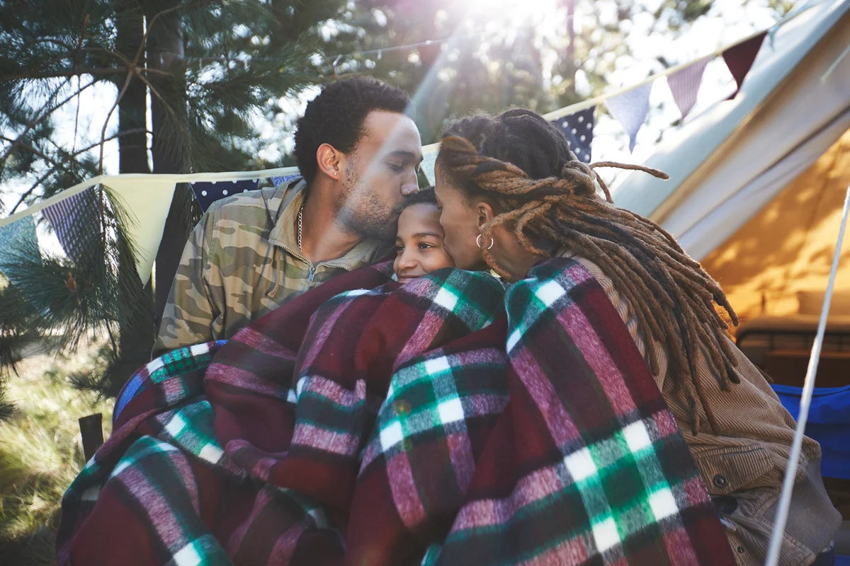 Happy parents kissing son, relaxing at campsite