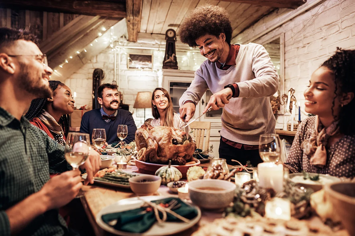 Young happy man carving Thanksgiving turkey during dinner party