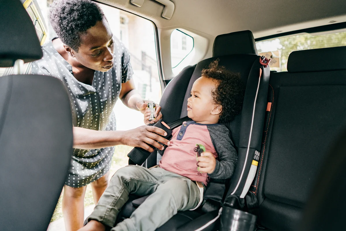 parent putting toddler in car seat