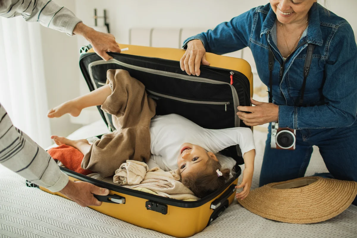 Happy family packing suitcase for summer vacation with toddler