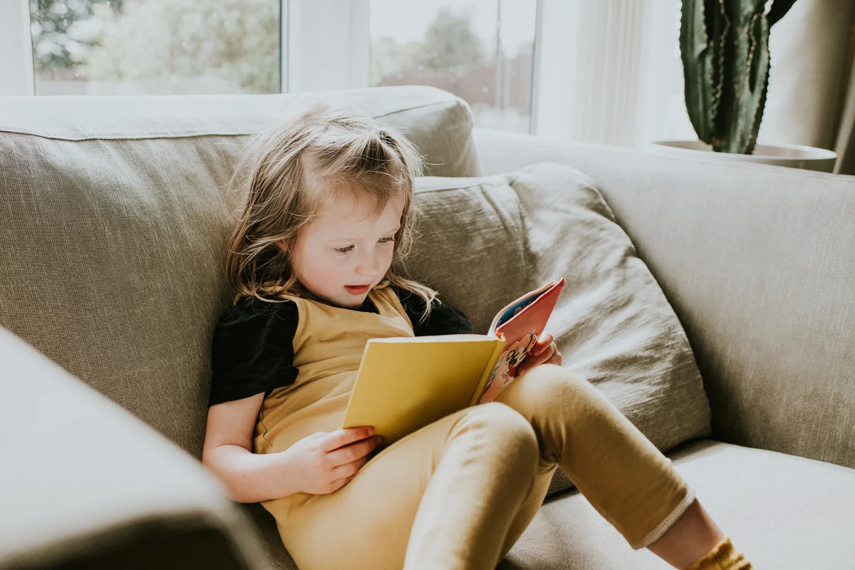 Cute little girl sitting on a chair reading a book