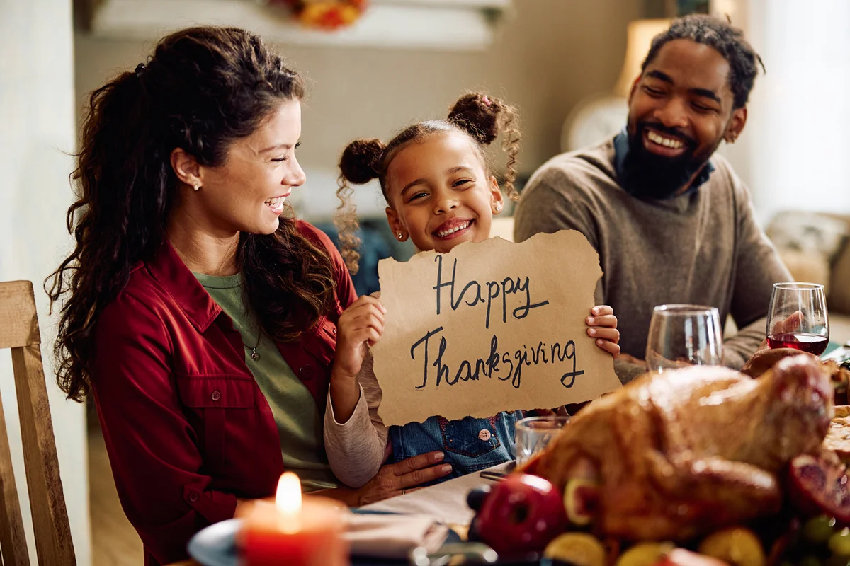 girl holding Happy Thanksgiving placard during family meal