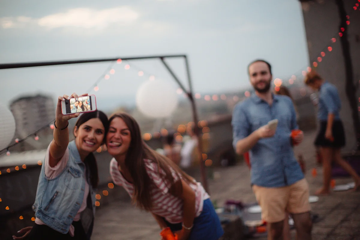 Couple of friends having a party on the rooftop of the building at sunset, making a selfie