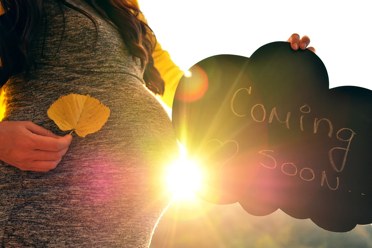 Pregnant woman holding a sign that says "Coming soon"