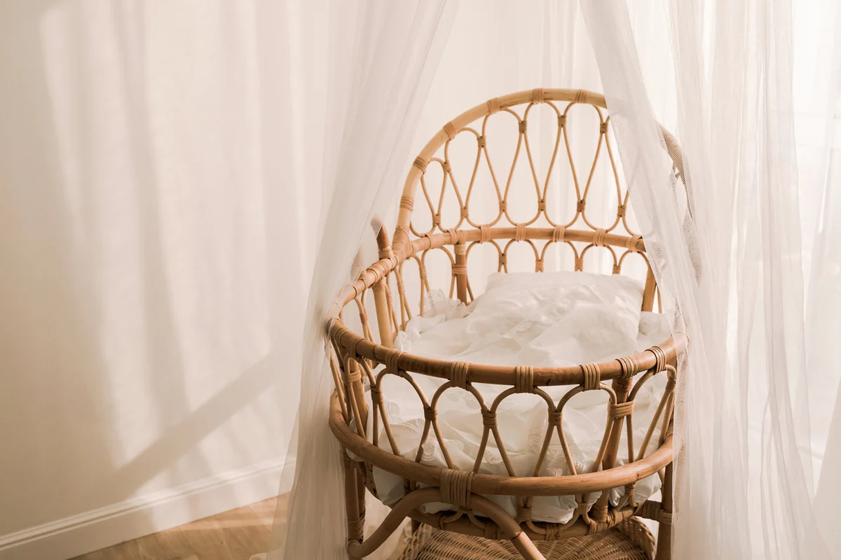 Stylish scandinavian newborn baby nursery with natural rattan cradle and sheer white canopy hanging over it.