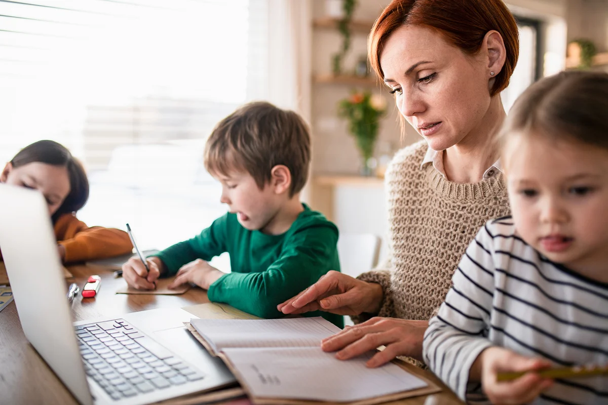 Mother of little children working on laptop when distance learning and doing artwork at home