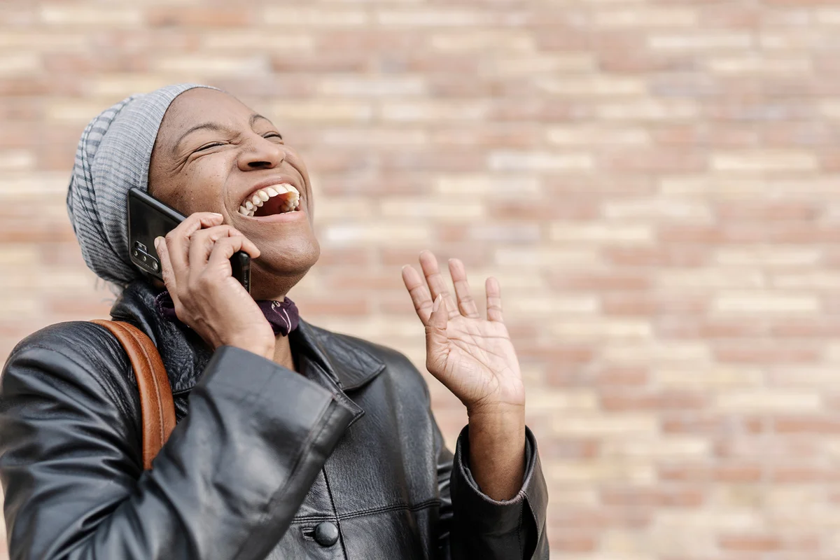 Happy woman laughing while talking on the phone outdoors on the street.