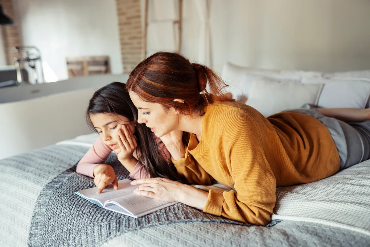 Mother and daughter reading book while lying on bed at home