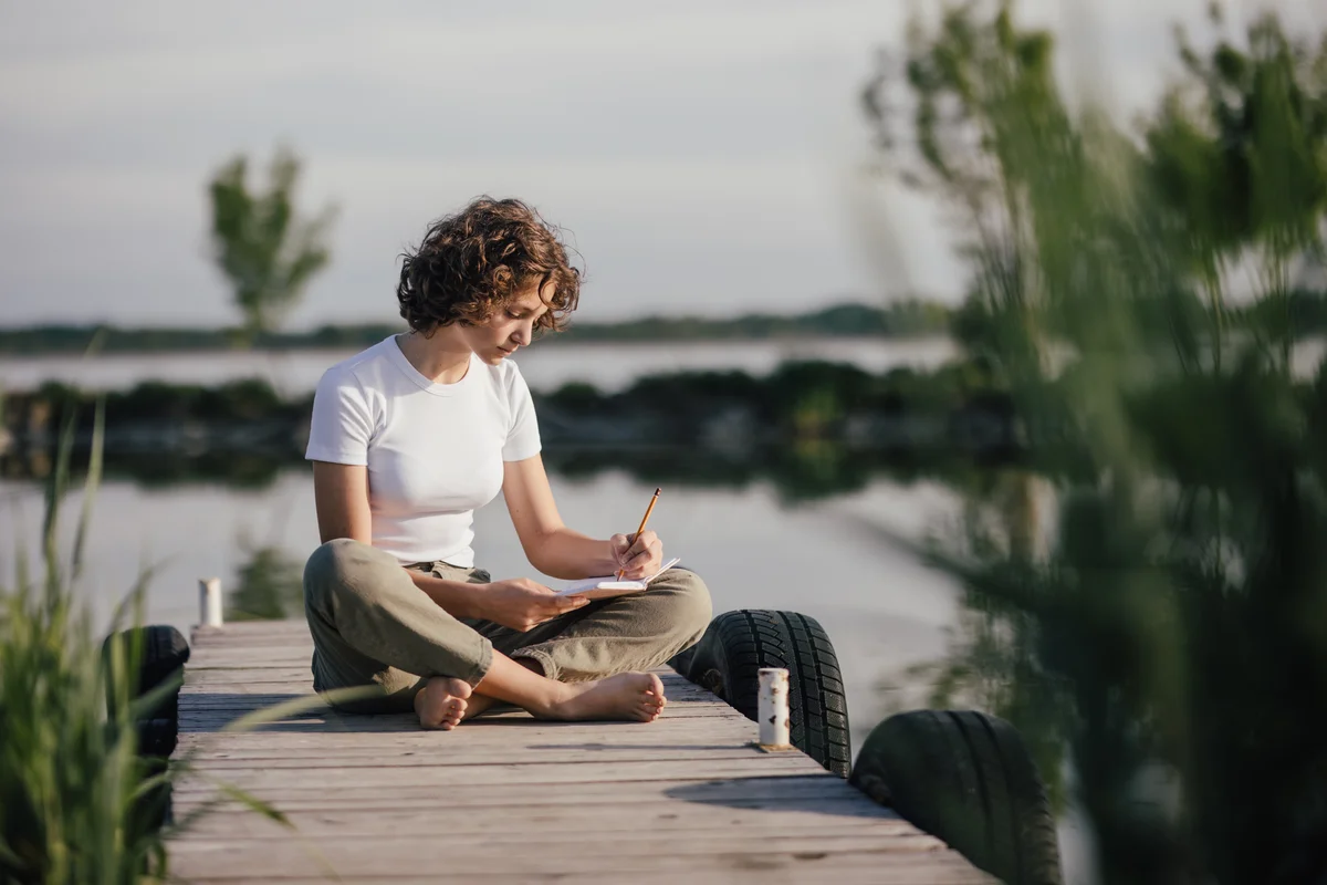 Young teenage girl sitting on pier and writing notes
