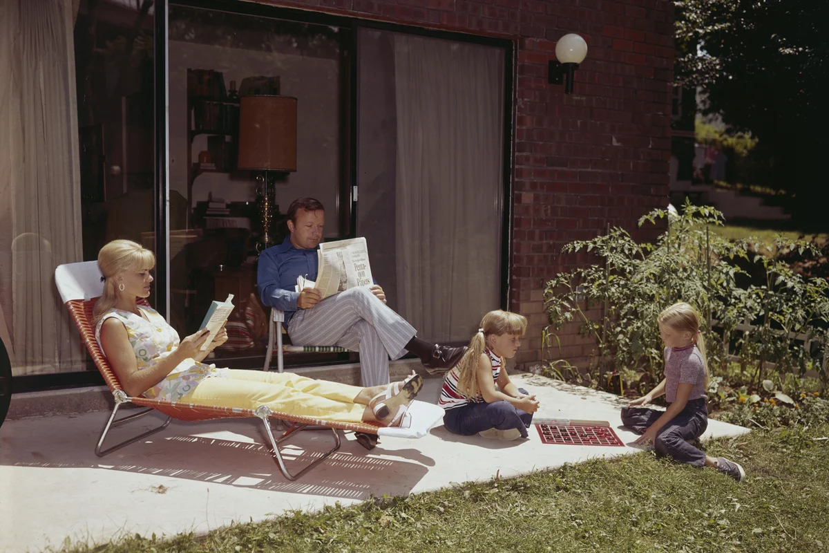 Parent and their two young daughters sunbathing on their patio, 1970 | Getty Editorial