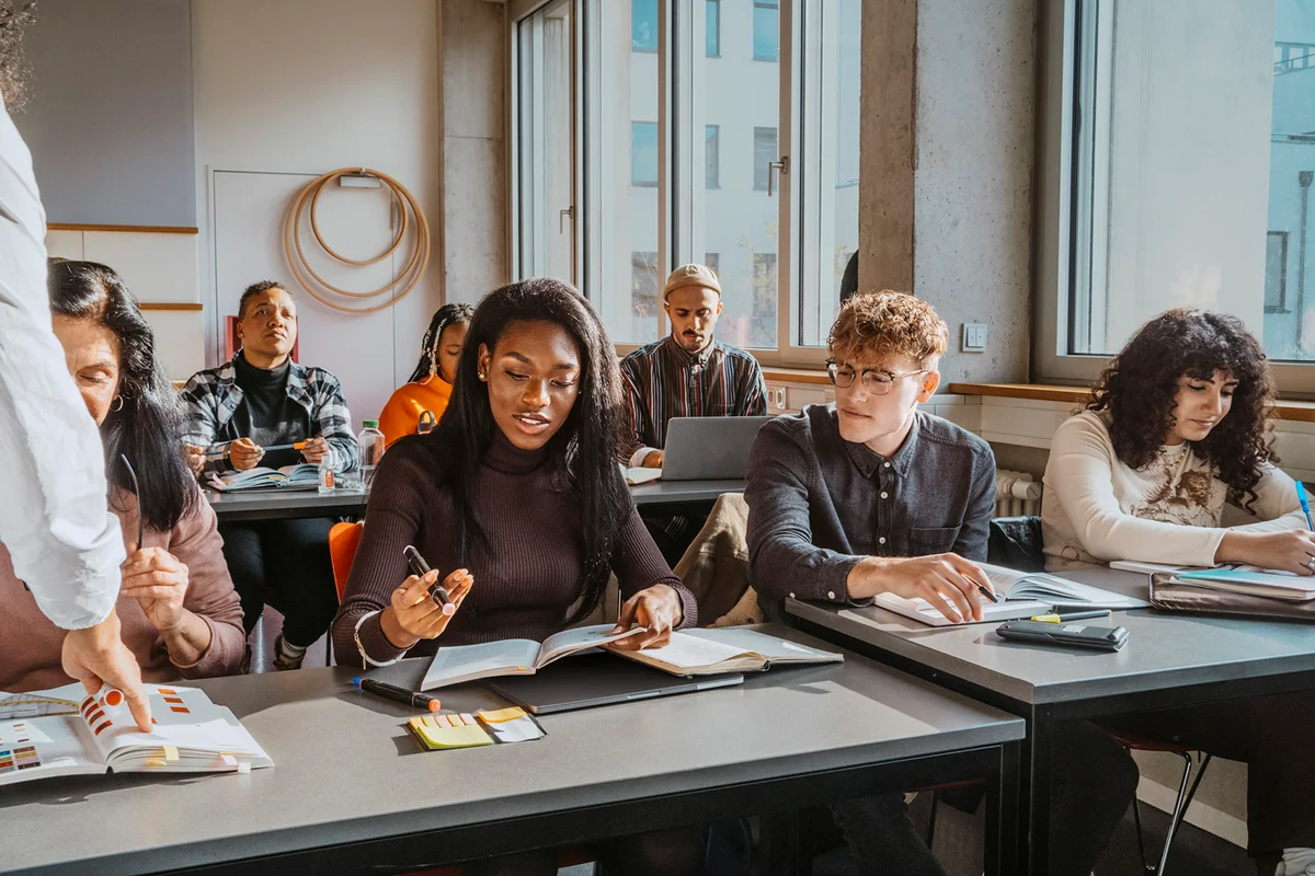students sitting at desk while learning from professor in classroom