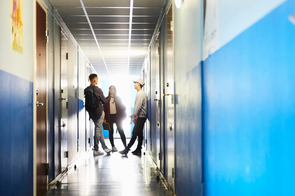 Full length of students talking while standing in corridor at university