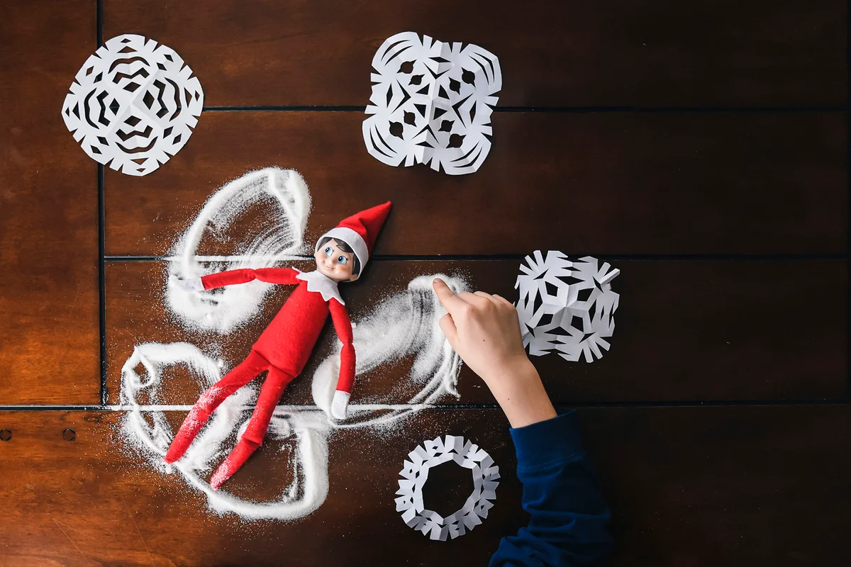 Overhead shot of child's arm playing with elf doll on a table