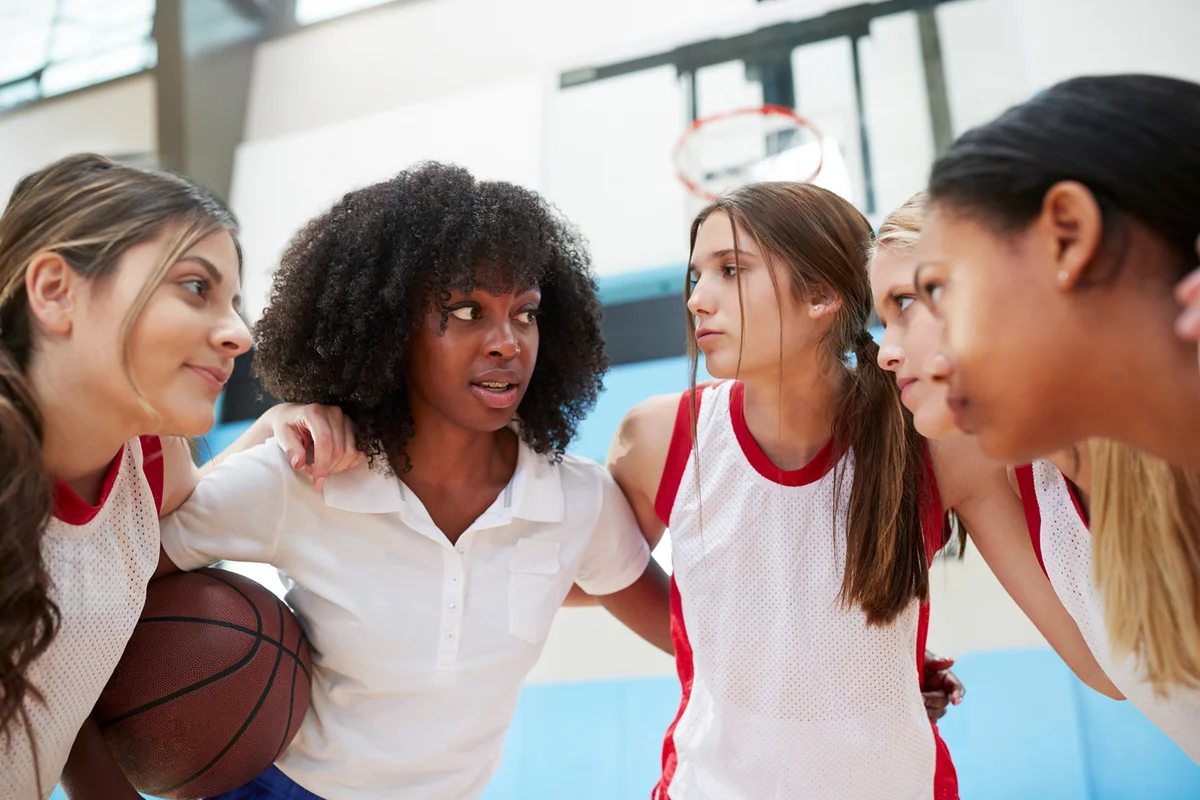 Female High School Basketball Players In Huddle Having Team Talk With Coach