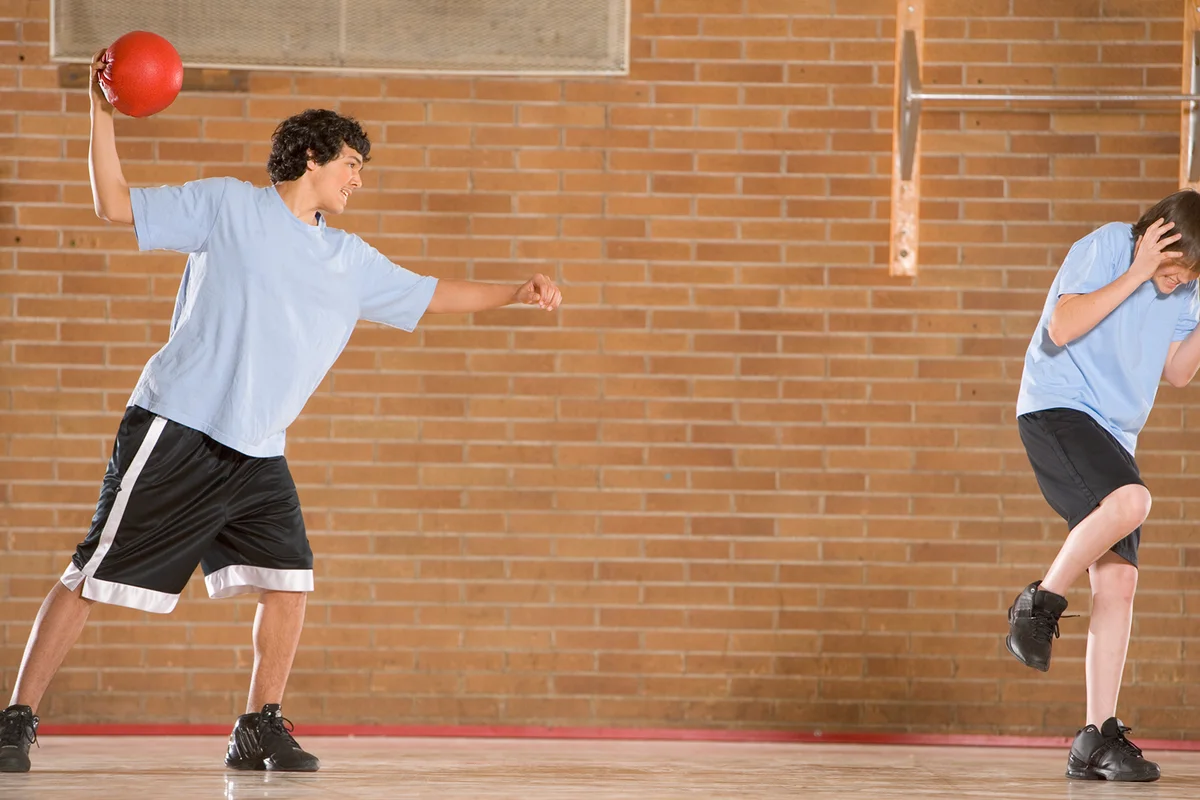 Boy (13-15) in gym throwing dodgeball at other boy