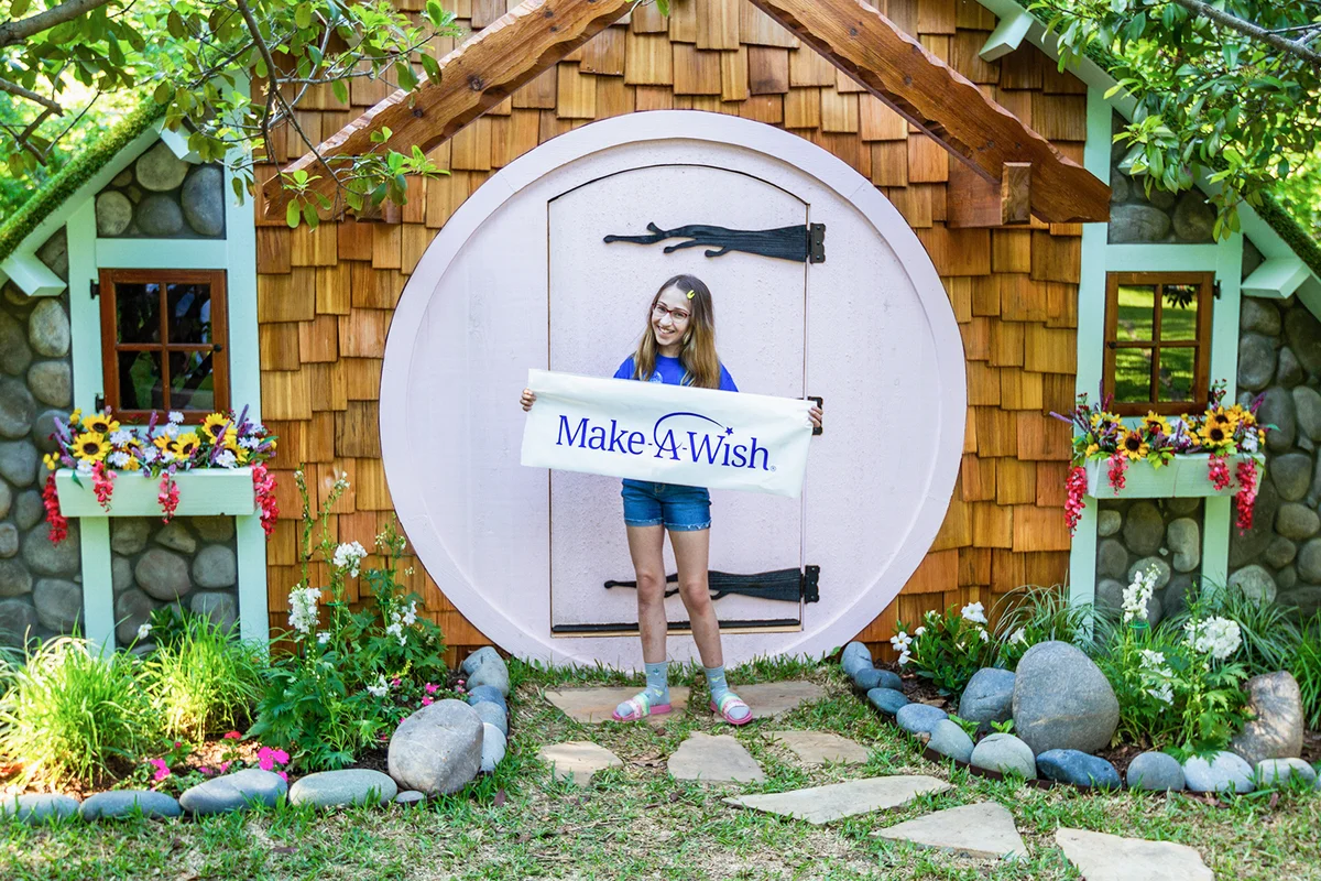 Image of a girl named Harper. Make-A-Wish image with girl in front of cottage holding Make-A-Wish