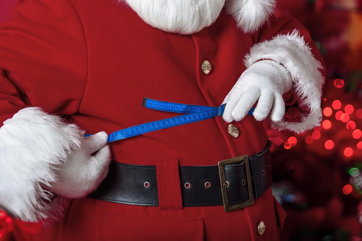 santa claus measures his fat belly with ribbon