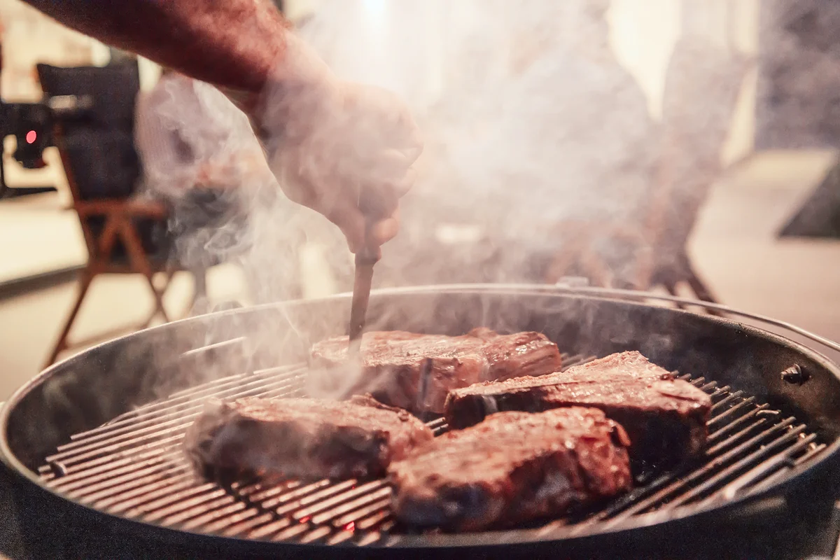 Meat being grilled while friends and family are waiting for a meal
