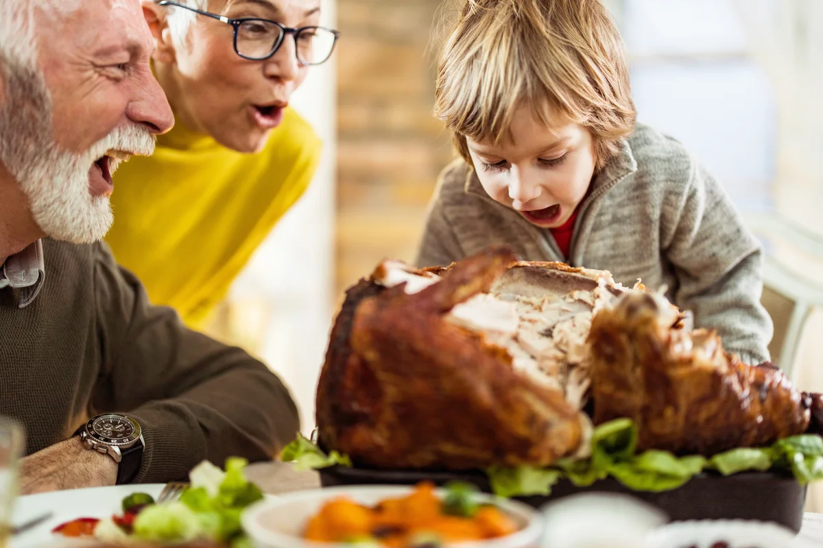 Little boy having fun while pretending to eat the whole Thanksgiving turkey at his grandparents