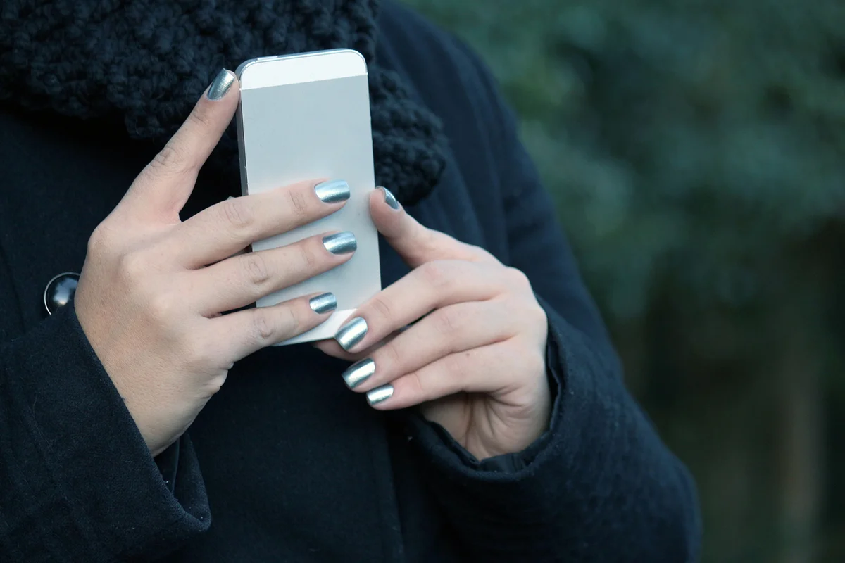 woman's hand with metal and perfectly painted nails holds a cell phone