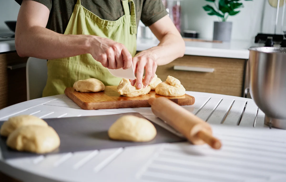 Baker in green apron dividing dough in parts, cutting dough with spatula