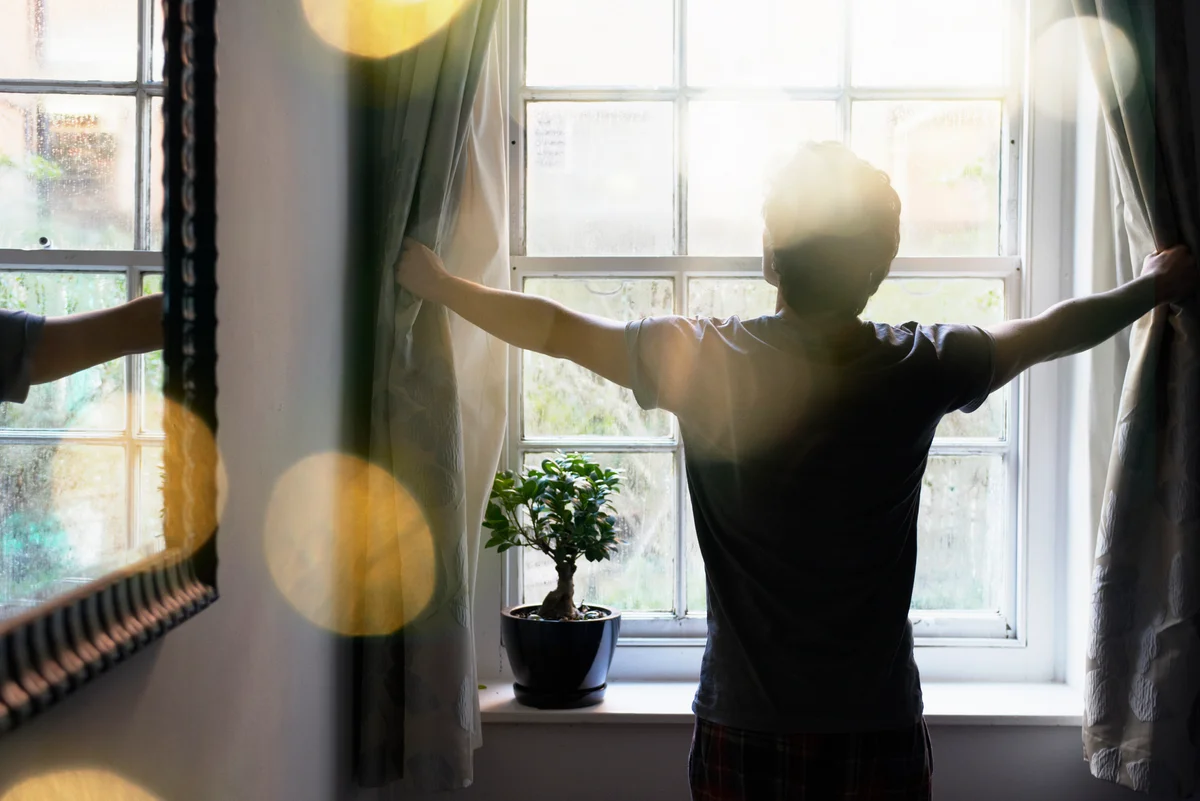 Man opening curtains in the morning