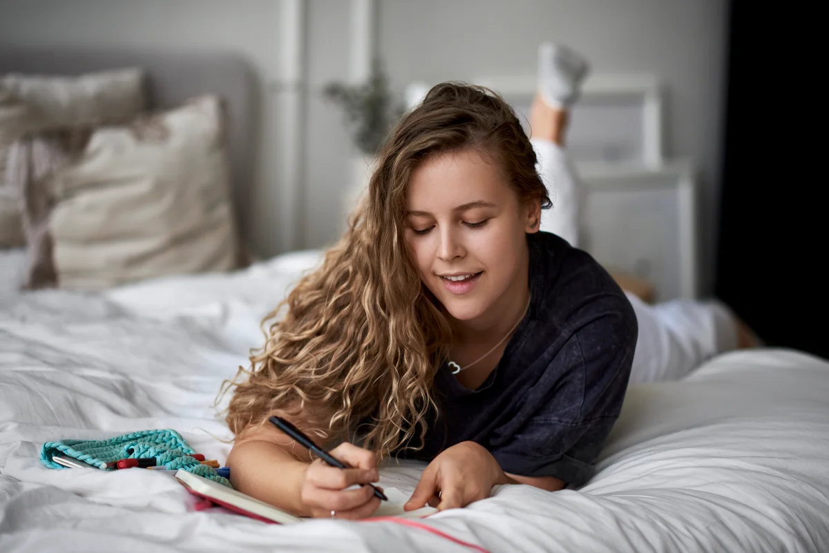 Young woman lying on bed writing in diary