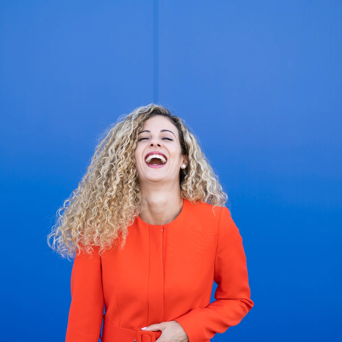 Portrait of laughing young woman wearing red dress in front of blue background