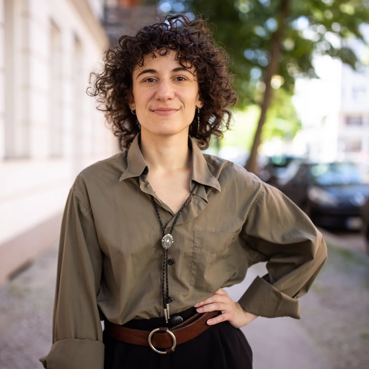 Confident non-binary person standing with hand on hip outdoors