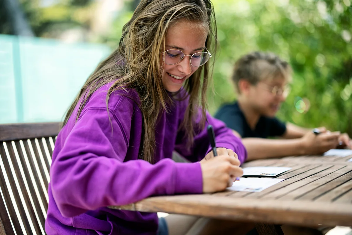 Teenagers sitting by the backyard table and writing postcards