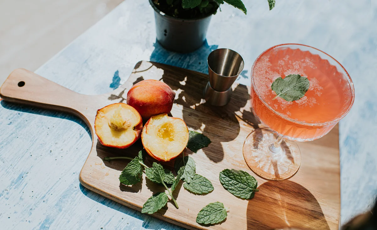 A peach flavoured drink sits on a wooden chopping board with fresh fruit