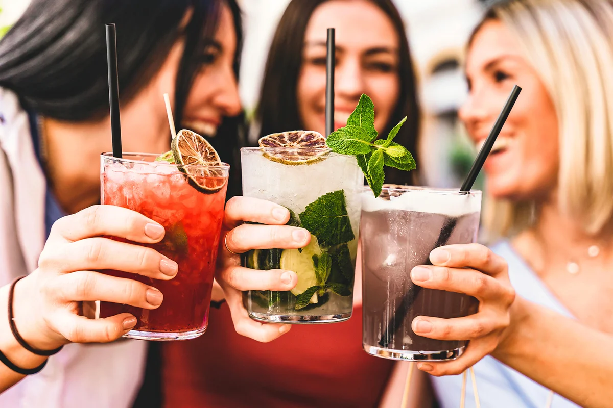 Group of happy friends toasting and drinking fancy cocktails at bar terrace
