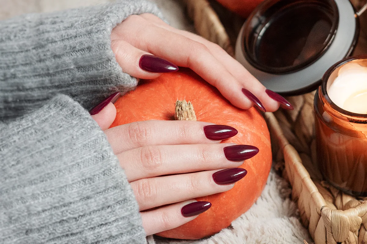 girl with a burgundy manicure holds a pumpkin