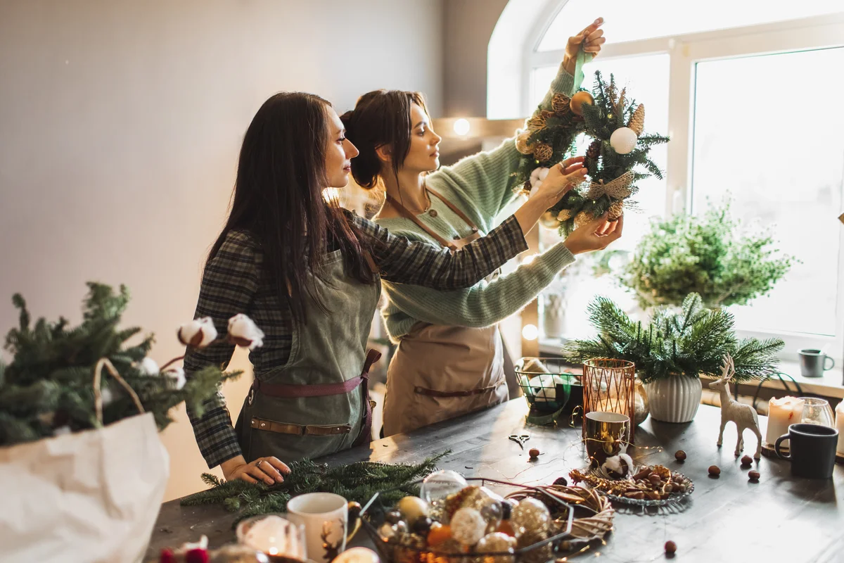 Two women making Christmas wreath using fresh pine branches and festive decorations