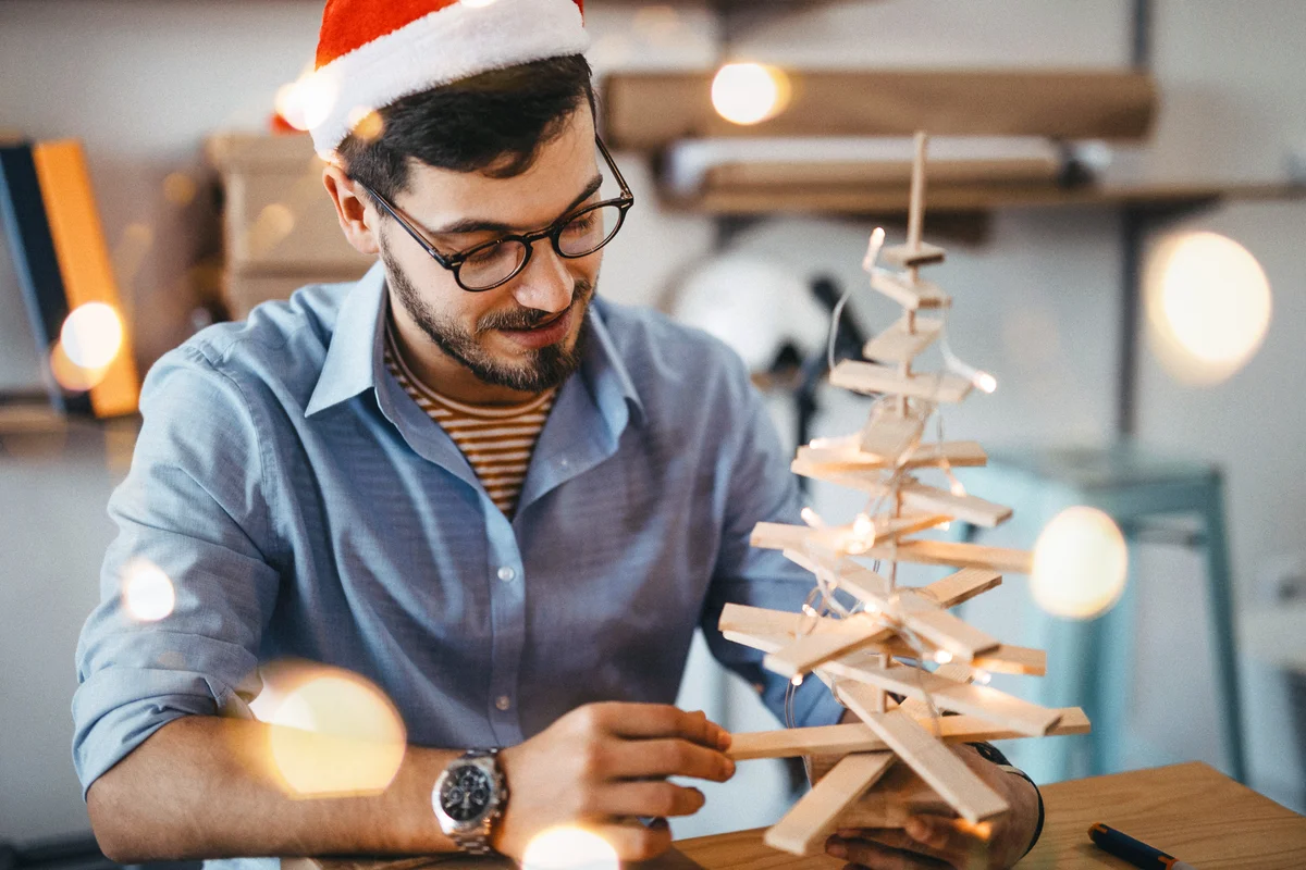 Man decorating wooden tree with Christmas lights