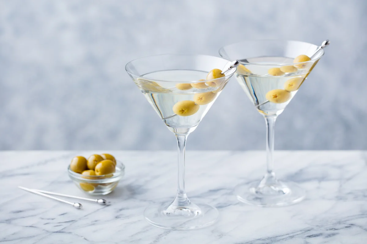 Martini cocktail with green olives on marble table background