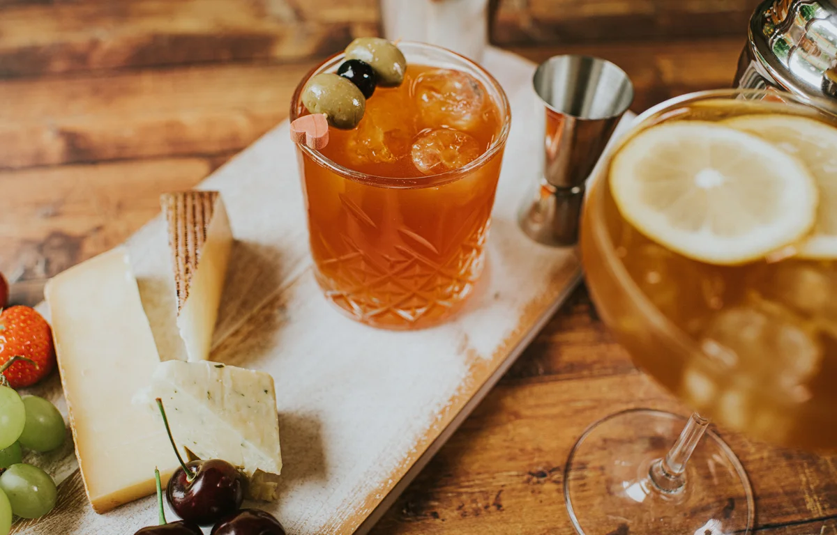 Delicious, simple cheese board and a fruity cocktails on a wooden table