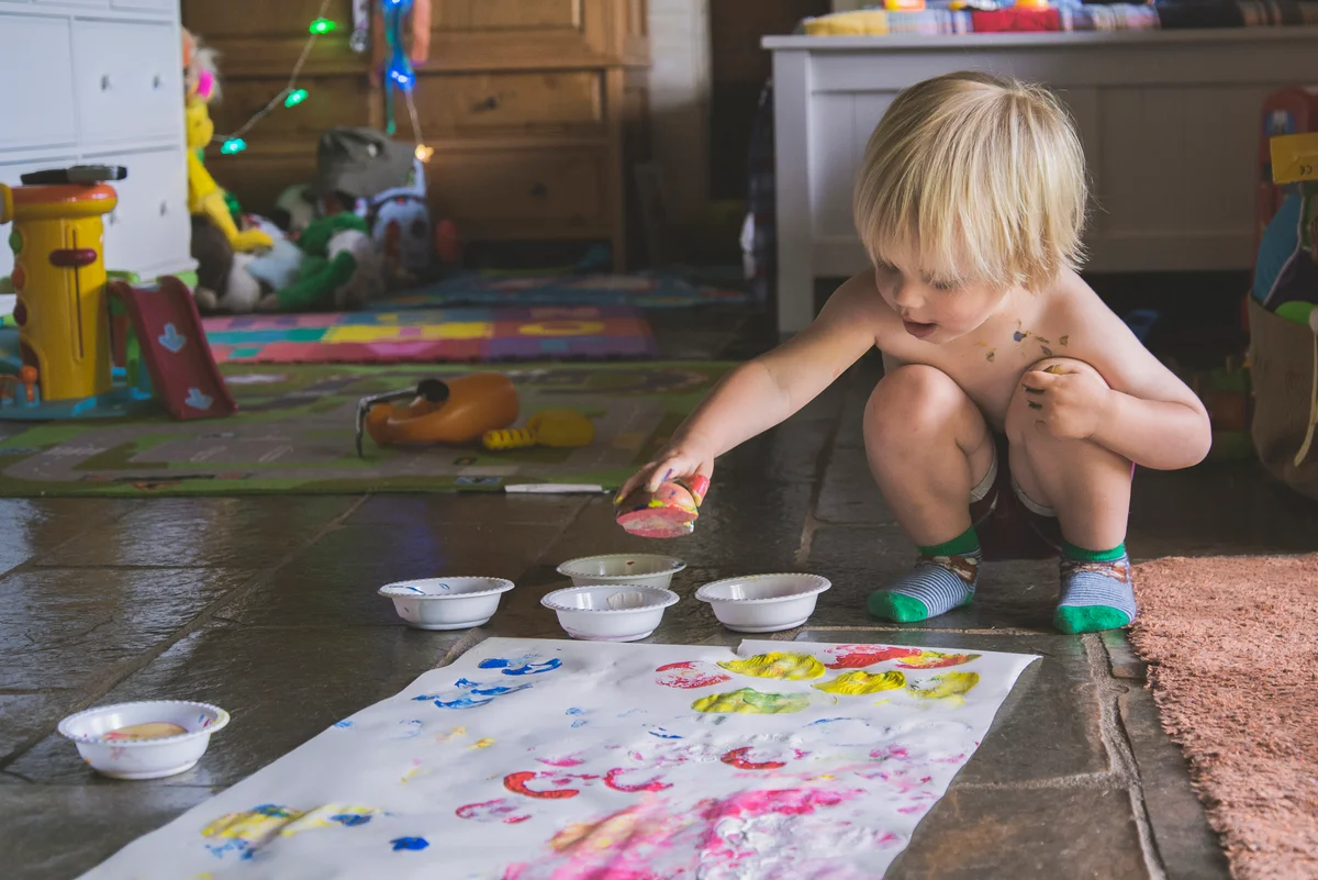 boy with watercolor paints making apple prints on white paper at home