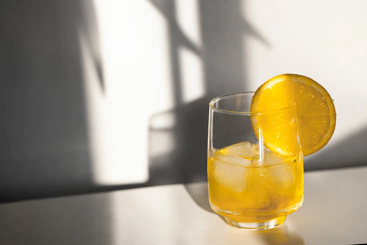 Alcohol cocktail with ice cubes on white background with hard light and shadow