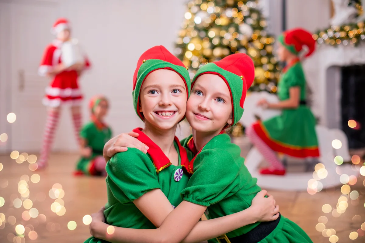 Two cheerful girls in Santa's elves costumes on the background of a Christmas play