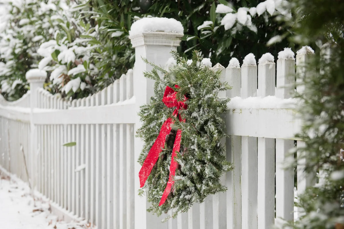 Christmas wreath hanging on white fence covered in snow