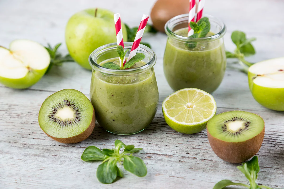 Two glasses of green smoothie and ingredients on wood