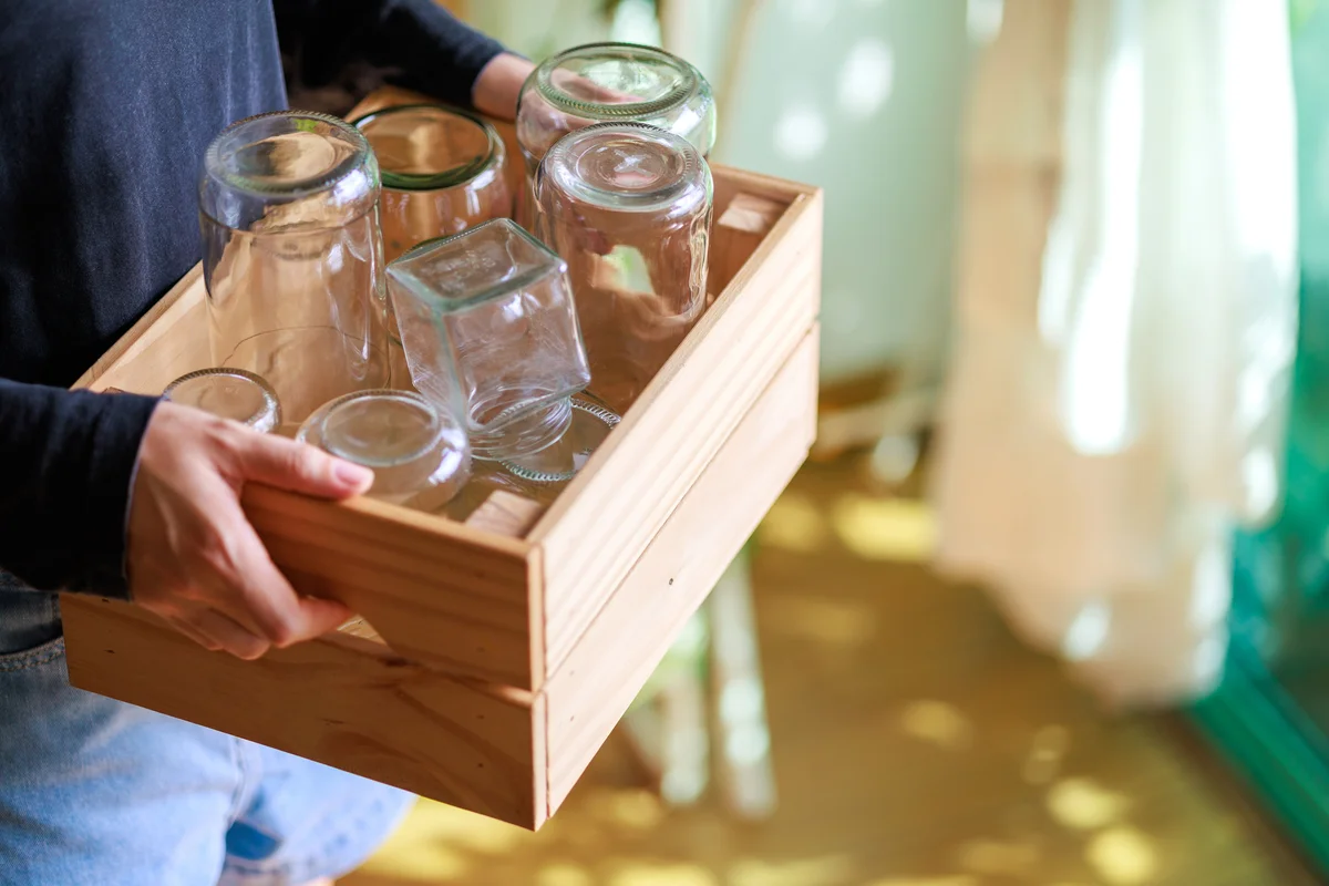 person placing empty glass jars into a wooden box