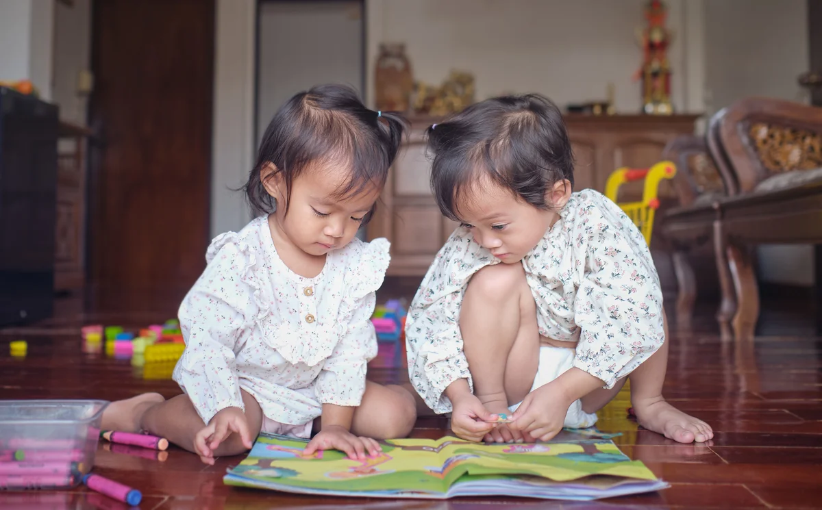 Sisters playing with crafts book with sticker at home