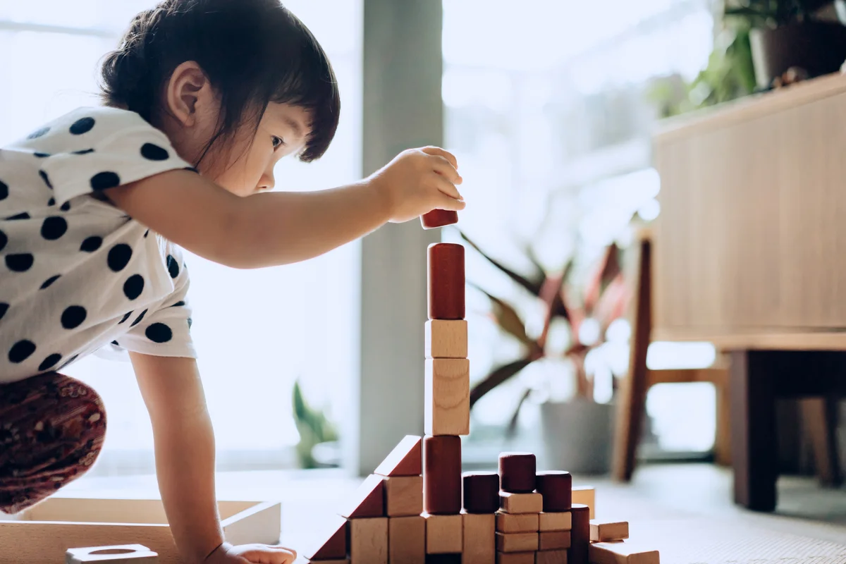 girl crouching on the floor playing with wooden building blocks at home
