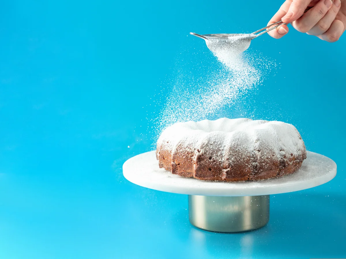 sprinkling powdered sugar on a bundt cake